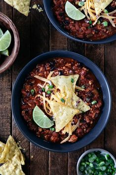 two bowls filled with chili, beans and tortilla chips on top of a wooden table