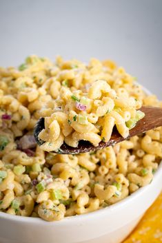 a wooden spoon full of macaroni salad on top of a yellow place mat