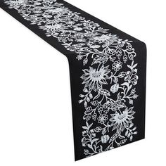 a black table runner with white flowers and leaves on the border, in front of a white background