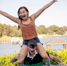 a woman is riding on the back of a man in front of a body of water