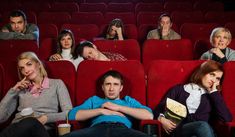 several people sitting in red seats with their mouths open and looking at the camera, while one person holds his hand on his chin