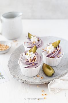 three cupcakes with purple frosting and toppings on a plate next to a mug