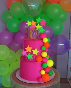 a pink birthday cake with stars on top and balloons in the background at a 10th birthday party