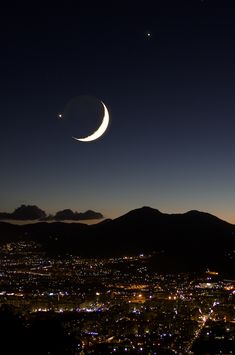 the moon and venus are seen in the night sky over a cityscape with mountains