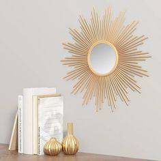 a gold sunburst mirror sitting on top of a wooden table next to books