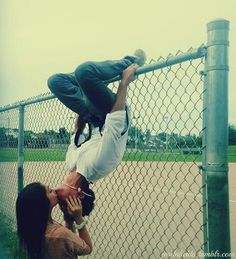 a man doing a handstand on top of another man in front of a fence