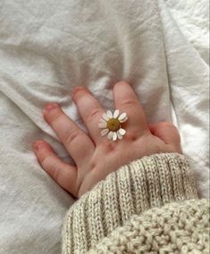 a person's hand with a small white flower on top of their finger, laying in bed