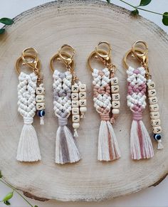 four key chains with tassels on top of a piece of wood next to flowers