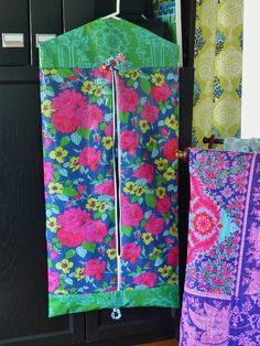 two pieces of colorful fabric hanging from hooks on the wall next to each other in front of a black cabinet