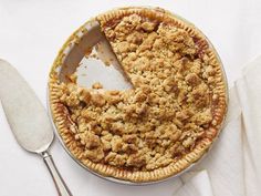 a pie with a slice missing from it on a white table cloth next to a fork and spoon