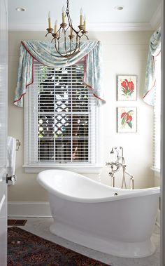 a white bath tub sitting in a bathroom next to a window with curtains on it