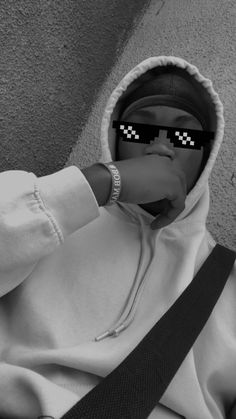 a person in a hoodie with sunglasses on their face and one hand over his mouth