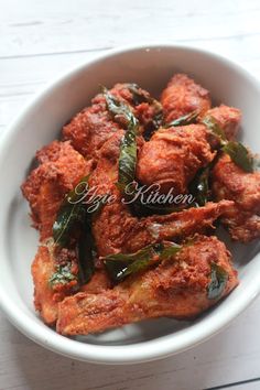 a white bowl filled with chicken wings and green peppers on top of a wooden table