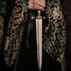 a person holding a large knife in their right hand and wearing a green jacket with gold trim