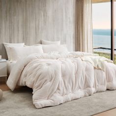 a bed with white comforter and pillows in front of a window overlooking the ocean