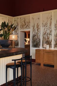 a bar with three stools in front of it and plants on the wall behind it