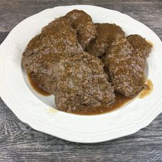 a white plate topped with meatballs covered in gravy on top of a wooden table