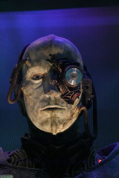 an alien man with goggles and headgear in front of a blue background