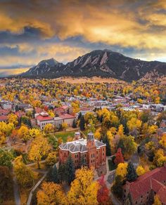 an aerial view of a city with mountains in the background and autumn foliage around it