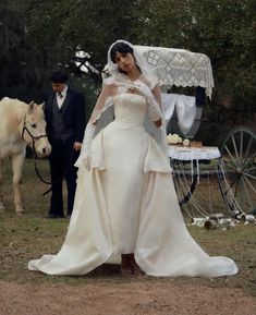 a woman in a white wedding dress standing next to a horse and man with a bridal gown