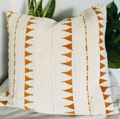 an orange and white pillow sitting on top of a bed next to a potted plant