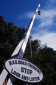 a railroad crossing stop sign with the sky in the backgrouund and trees in the background