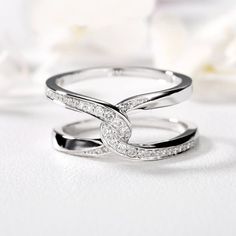 two white gold wedding rings with diamonds on top and in the middle, sitting next to a flower