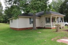 a small white house sitting on top of a lush green field next to a tree