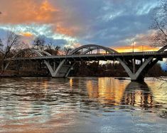 a bridge that is over some water with trees in the background and clouds in the sky