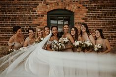 a group of women standing next to each other in front of a brick wall holding bouquets