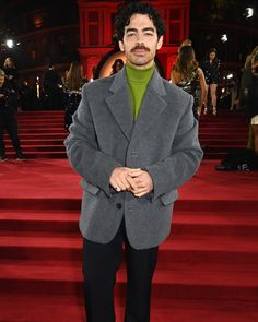 a man in a gray jacket and green turtle neck sweater standing on red carpeted steps