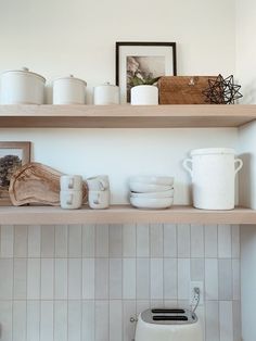 the shelves in the kitchen are filled with white dishes and cups, including one that is on top of a toaster