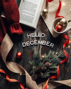 an open book on top of a wooden table with christmas decorations and ribbon around it