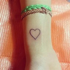 a small heart tattoo on the wrist with braids and a green ribbon around it