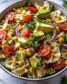 a bowl full of pasta salad with tomatoes, corn and avocado on top