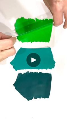 two hands holding green and blue paint over white paper