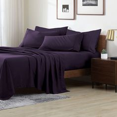 a bed with purple sheets and pillows in a room