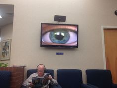 a man sitting on a blue chair in front of a tv with an eye looking at him