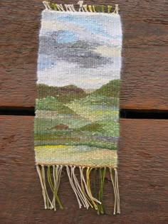 a close up of a piece of cloth on a wooden surface with grass and mountains in the background