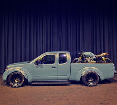 a blue pick up truck parked in front of a curtained wall with a motorcycle on the back