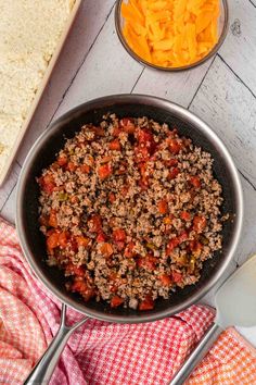 a pan filled with ground beef and carrots next to a bowl of cheese on the side