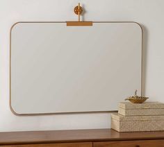 a mirror sitting on top of a wooden dresser next to a stack of folded books