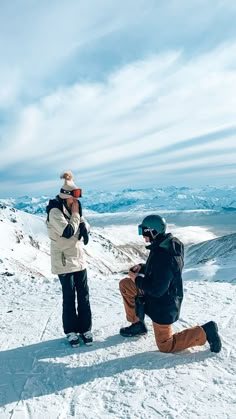 two people sitting in the snow on top of a mountain