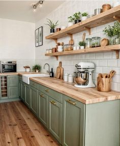 a kitchen with green cabinets and wooden counter tops is pictured in this image, there are plants on the shelves above the sink