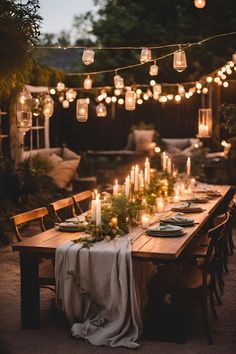 an outdoor dinner table with candles and greenery on the table, surrounded by hanging lanterns