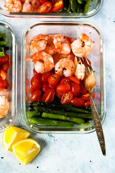 two plastic containers filled with shrimp, asparagus and tomatoes next to lemon wedges