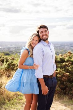 a man and woman standing next to each other on top of a hill