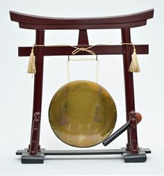 a gong in a wooden frame with two bells hanging from it's sides and a black object on the other side