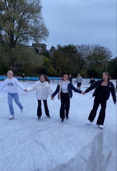 four people are skating on an ice rink in the wintertime with their arms outstretched