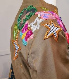 a woman's jacket with colorful sequins and stars on the back, sitting on a mannequin